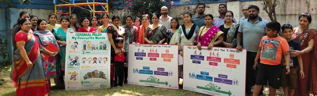 F-words-India2 A group of adults and children stand outdoors, holding educational posters about cerebral palsy awareness and communication strategies.