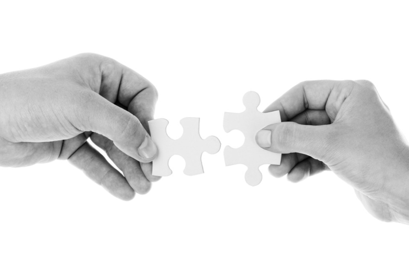Two hands each hold a puzzle piece, bringing them together as if to connect the pieces against a plain white background.