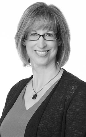 Campbell_Wenonah A woman with straight, shoulder-length hair and glasses smiles at the camera. She is wearing a necklace, a light top, and a dark cardigan. The background is plain white.