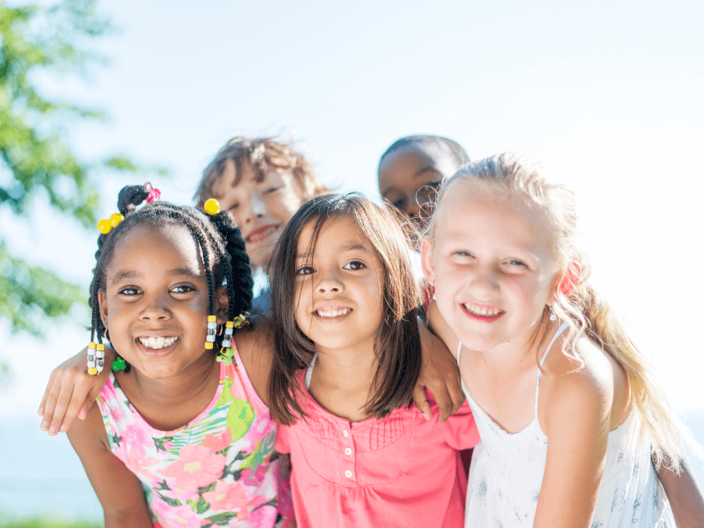 Copy of F-words module website banner (1024 × 768 px) (1) Five smiling children pose closely together outdoors on a sunny day, with greenery visible in the background.