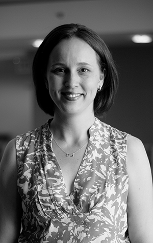 Cunningham_cropped A woman with short hair, wearing a patterned sleeveless blouse and necklace, smiles while standing indoors. The photo is in black and white.