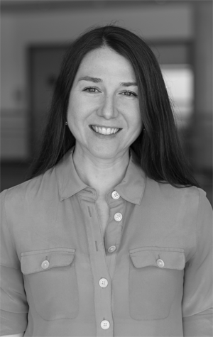 Dayle_cropped A woman with long dark hair, wearing a button-up shirt, smiles at the camera in a black and white photo.