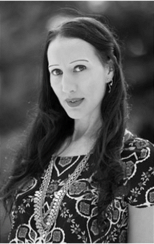 J_cropped_2 Black and white portrait of a woman with long dark hair wearing a patterned top and layered necklaces, looking at the camera.