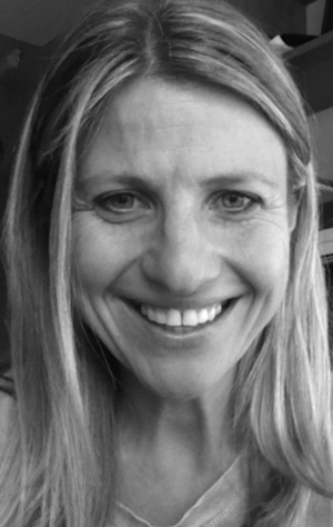 A woman with long, straight hair smiles at the camera in a close-up, black-and-white photo.