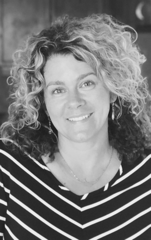 Laura-Turner Black and white photo of a woman with curly hair, wearing a striped top and earrings, smiling at the camera.