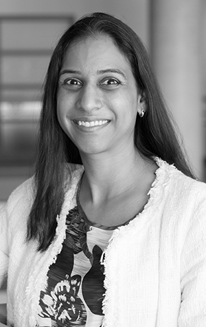 Phoenix_cropped A woman with long dark hair, wearing a light-colored jacket and patterned top, smiles at the camera in an indoor setting.