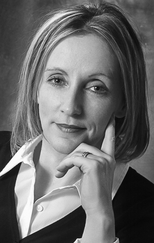 Sheila_Bennett-cropped Black-and-white portrait of a woman with shoulder-length hair, wearing a white collared shirt and dark vest, resting her chin on her hand.
