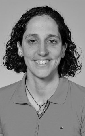 chantalCamden_croppedBW A person with short curly hair is smiling, wearing a collared shirt and a necklace. The photo is in black and white.