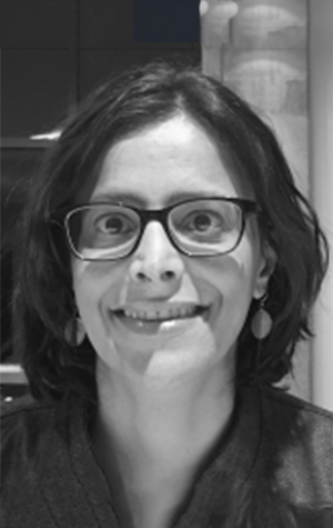 dana-anabyBW A woman with short dark hair and glasses smiles at the camera. She is wearing earrings and a dark top. The image is in black and white.