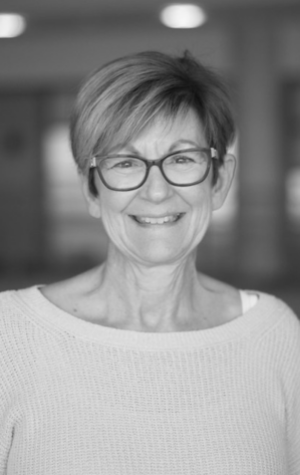 kathy A woman with short hair and glasses smiles at the camera while wearing a light-colored sweater. The image is in black and white.