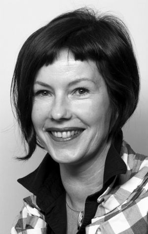 piskurb_Zuyd Black and white photo of a woman with short, dark hair, smiling, wearing a checkered shirt and a dark-collared jacket.