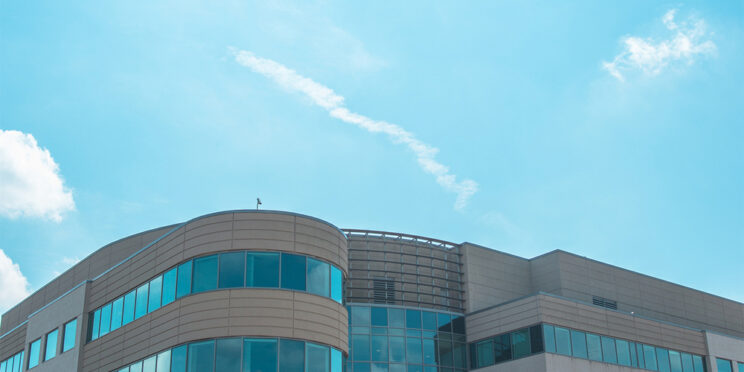 IAHS A modern three-story office building with large glass windows, people walking outside, and a bright blue sky overhead.
